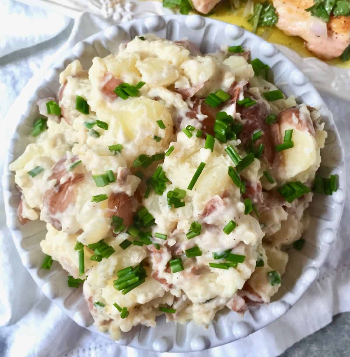 Rustic mashed potatoes in a white serving bowl garnished with chopped chives.