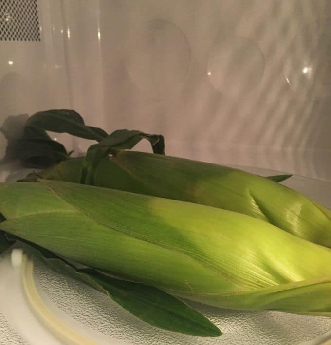 Two ears of corn cooking in the microwave. 