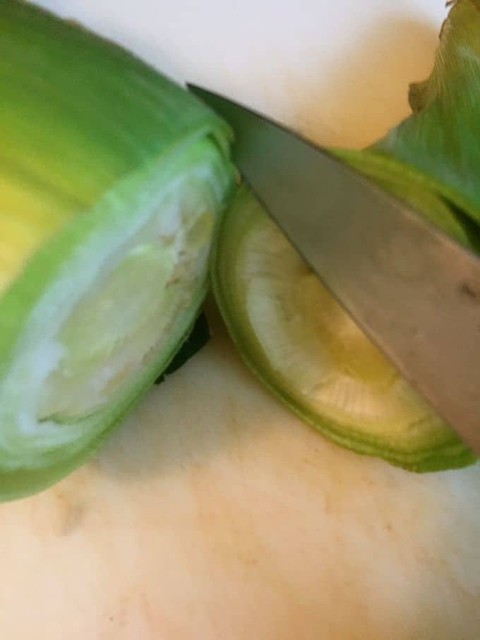 Using a knife to cut the stem of an ear of corn off after microwaving.