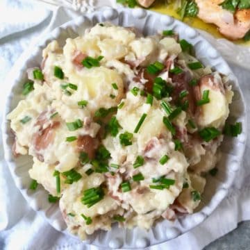 A large bowl of rustic mashed potatoes garnished with fresh chives.