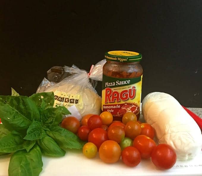 A bunch of fresh basil, pizza dough and sauce and cherry tomatoes on a cutting board. 