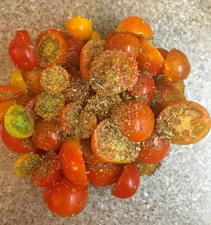 Sliced cherry tomatoes topped with dried herbs in a bowl. 