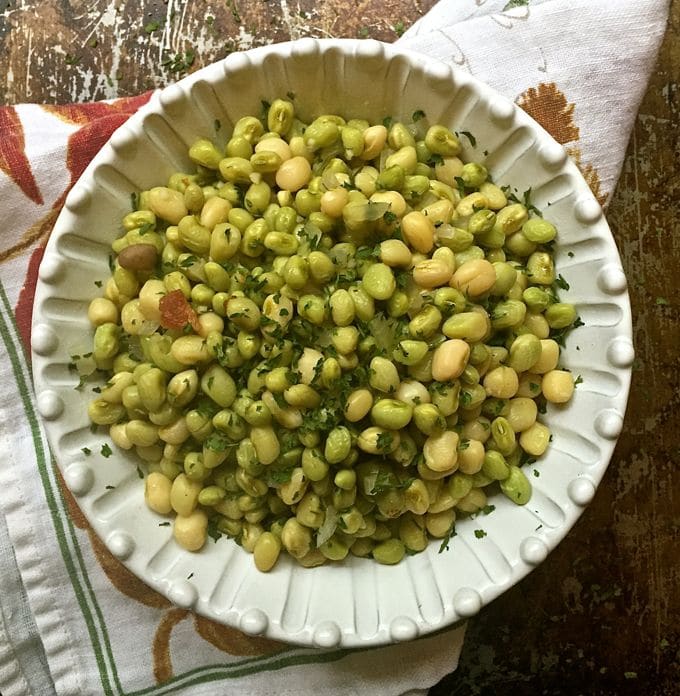 A white bowl full of peas resting on a kitchen towel.