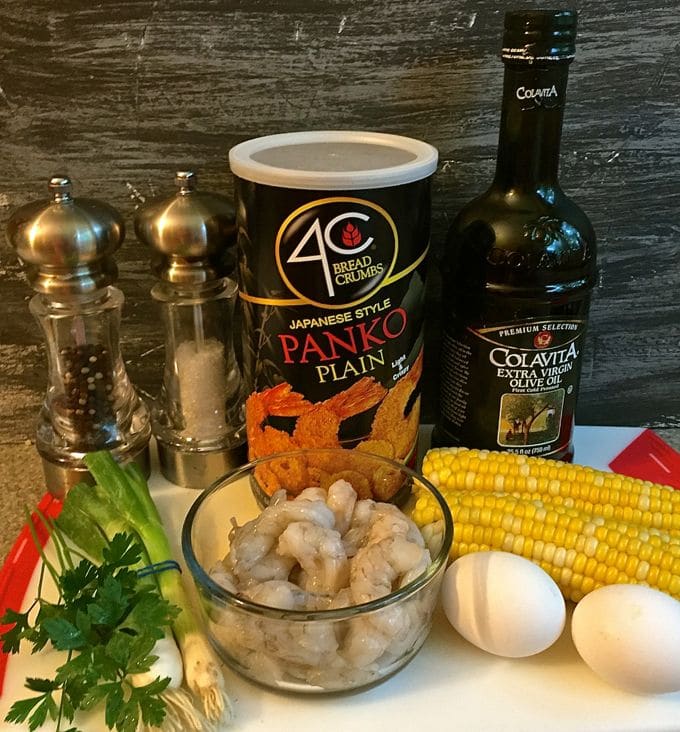 A bowl of raw shrimp, panko bread crumbs, two ears of corn and two eggs on a kitchen counter. 