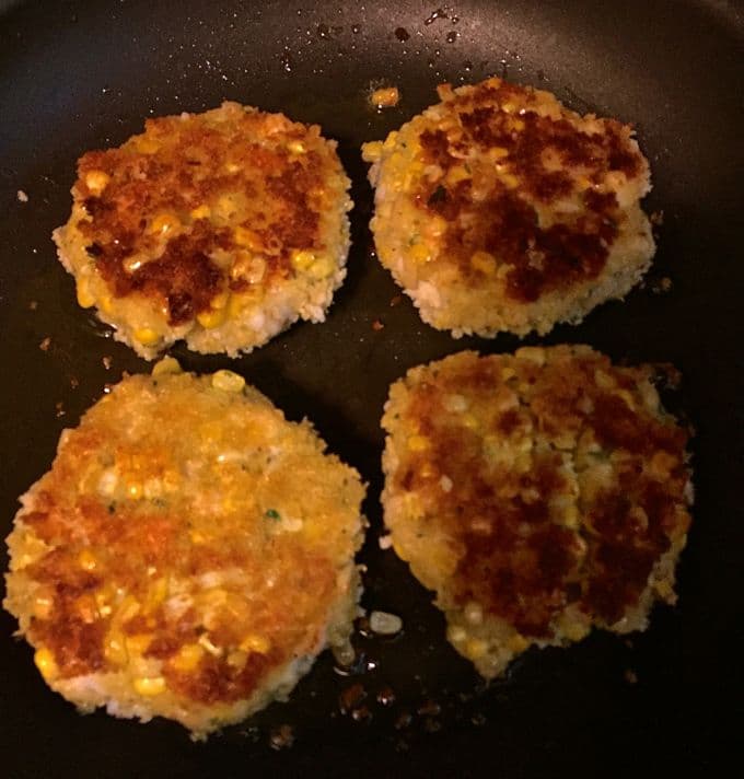 Four shrimp and corn fritters cooking in a skillet. 