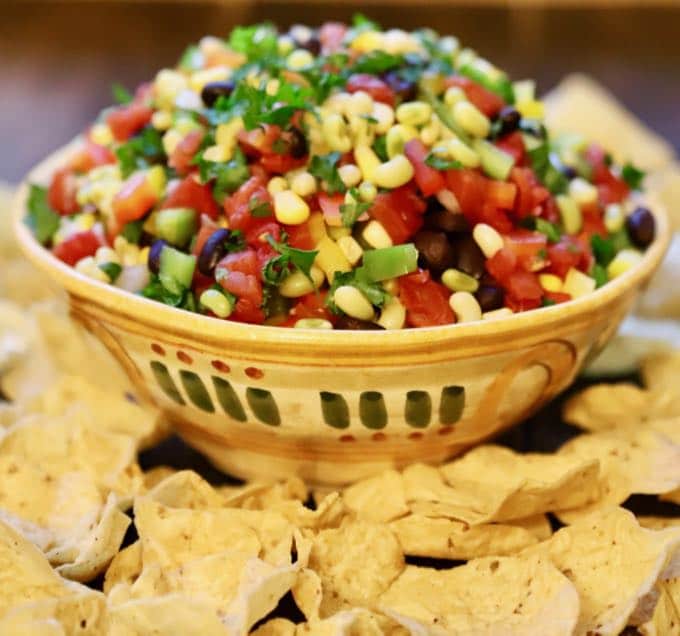 A pottery bowl full of diced tomatoes, fresh white acre peas, red and green bell pepper, and black beans. It's surrounded by tortilla chips. 