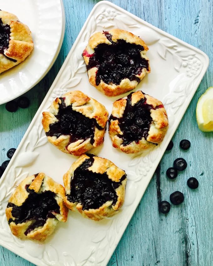 A white serving platter with four mini blueberry hand pies.