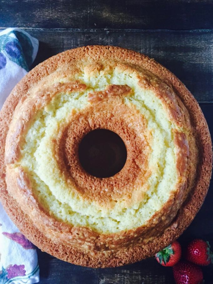 A pound cake cooling on a cutting board next to some sliced strawberries. 