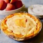 A peach pie in a clear glass pie plate ready to serve with a stack of plates.