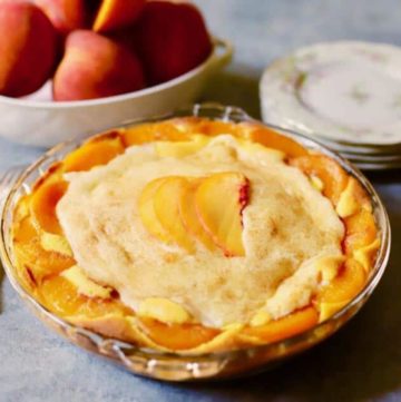 A peach pie in a clear glass pie plate ready to serve with a stack of plates.