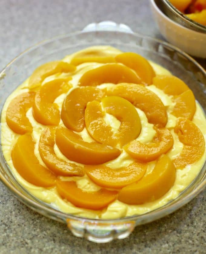 A layer of batter topped by a layer of peaches in a pie dish.