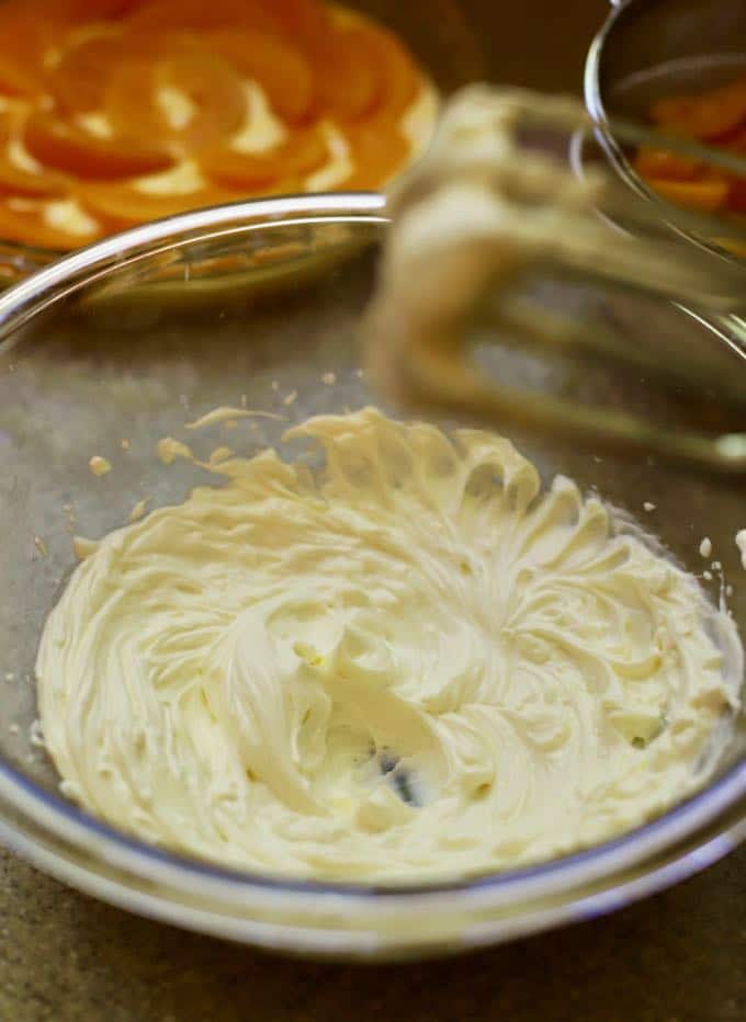 Cream cheese and heavy cream being mixed with an electric mixer.