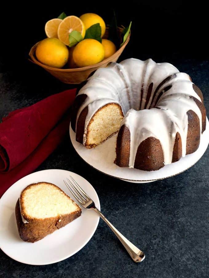 A lemon bundt cake with lemon glaze with lemons in the background.