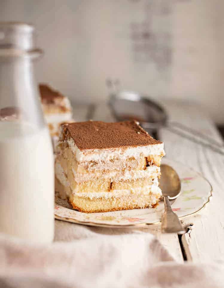 A piece of tiramisu cake on a plate with a bottle of milk.