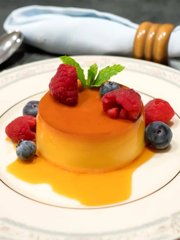 Sous Vide Creme Caramel on a white plate topped with caramel sauce and fresh fruit. 