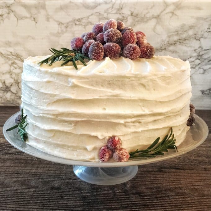 Italian Cream Cake on a cake plate covered with white icing and topped with fresh strawberries. 