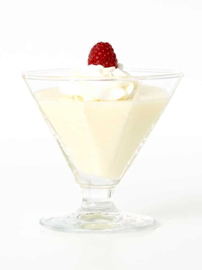 Lemon Posset on a glass dessert bowl topped with whipped cream and a raspberry. 