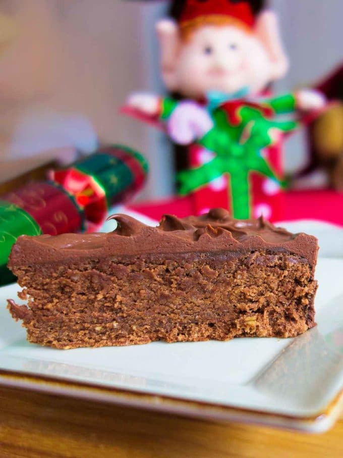 A slice of Reine de Saba, or chocolate almond cake on a white plate with Christmas elves in the background. 