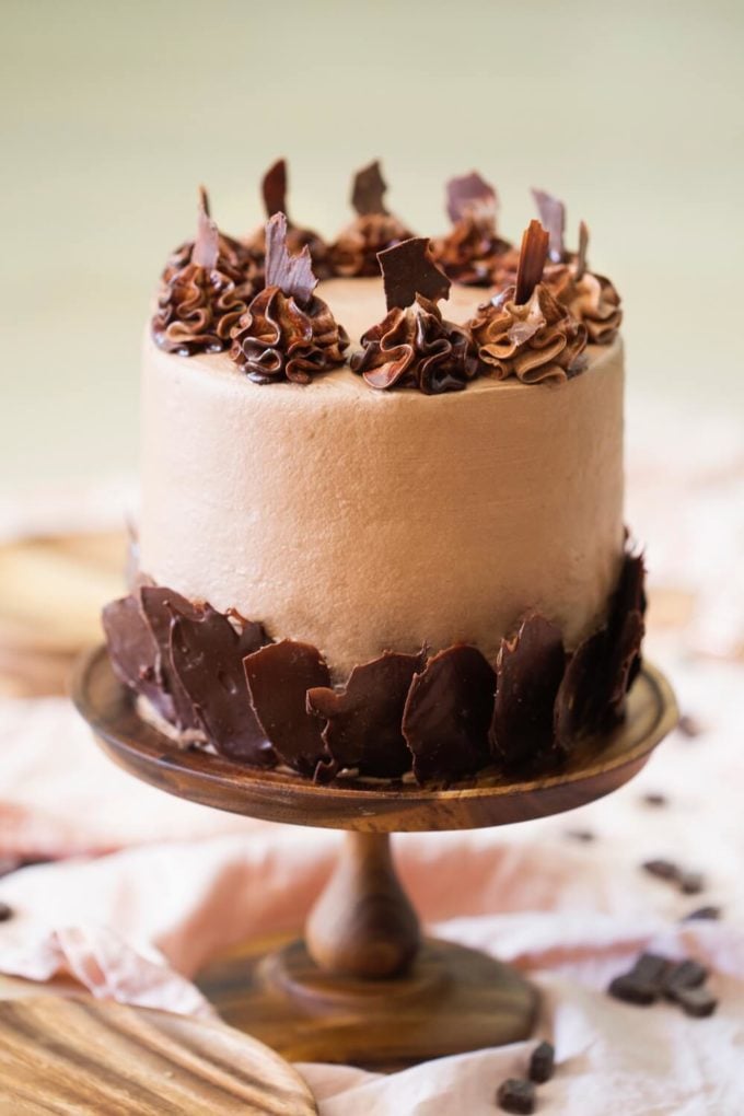 Triple Chocolate Cake on a wooden cake stand garnished with thin pieces of chocolate. 