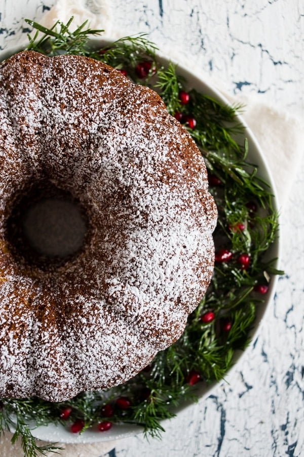 Cream Sherry Bundt Cake on a cake platter topped with powdered sugar and garnished with greenery and red berries.