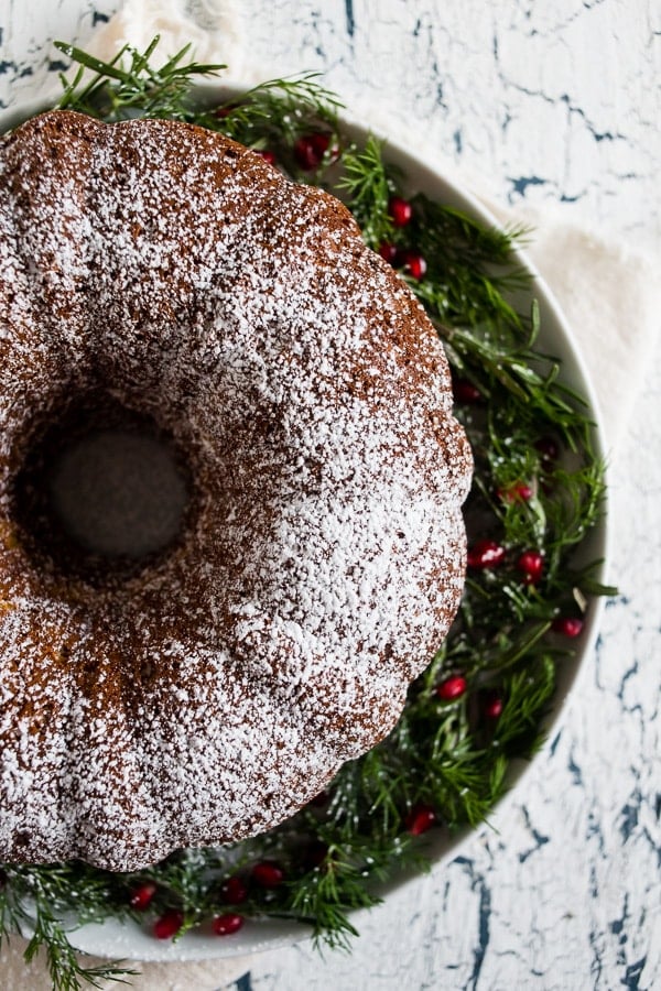 Cream Sherry Bundt Cake on a cake platter topped with powdered sugar and garnished with greenery and red berries. 