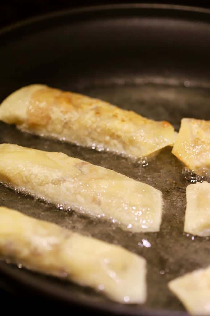 Egg rolls frying in a skillet. 