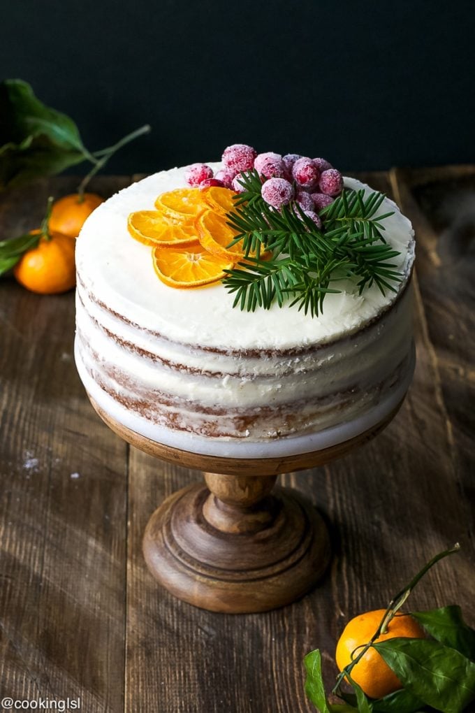 Tangerine Cake on a wooden cake stand topped with sliced tangerines and cranberries. 