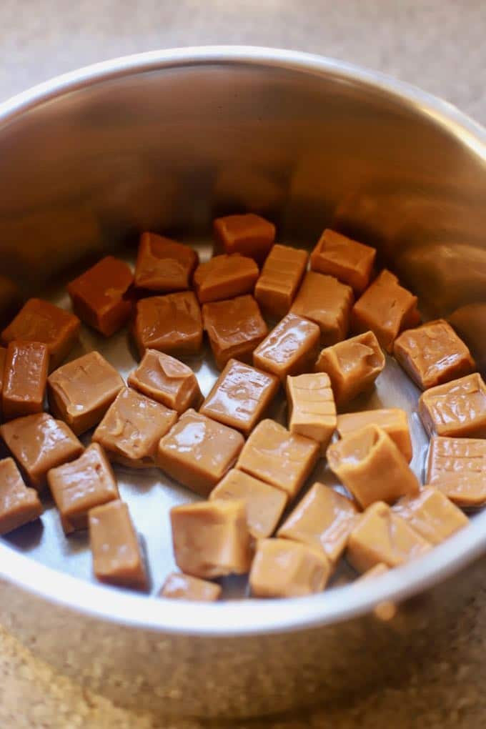 Melting caramels in a saucepan to make homemade Christmas candy.
