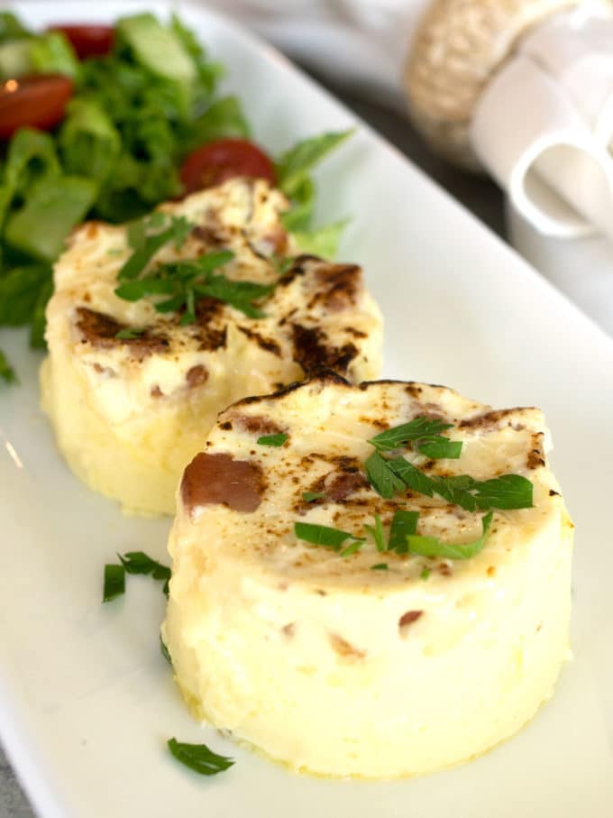 Two Sous Bide Bacon and Egg Cups on a plate topped with chopped parsley. 