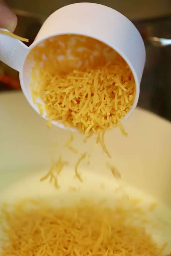Adding shredded cheese to a white sauce in a large saucepan.