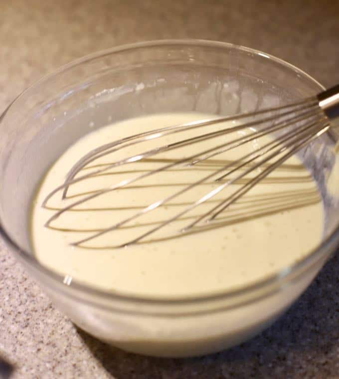 Using a whisk to mix up pancake batter in a clear glass bowl.
