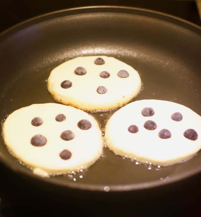 Blueberry pancakes cooking in a skillet on the stove.