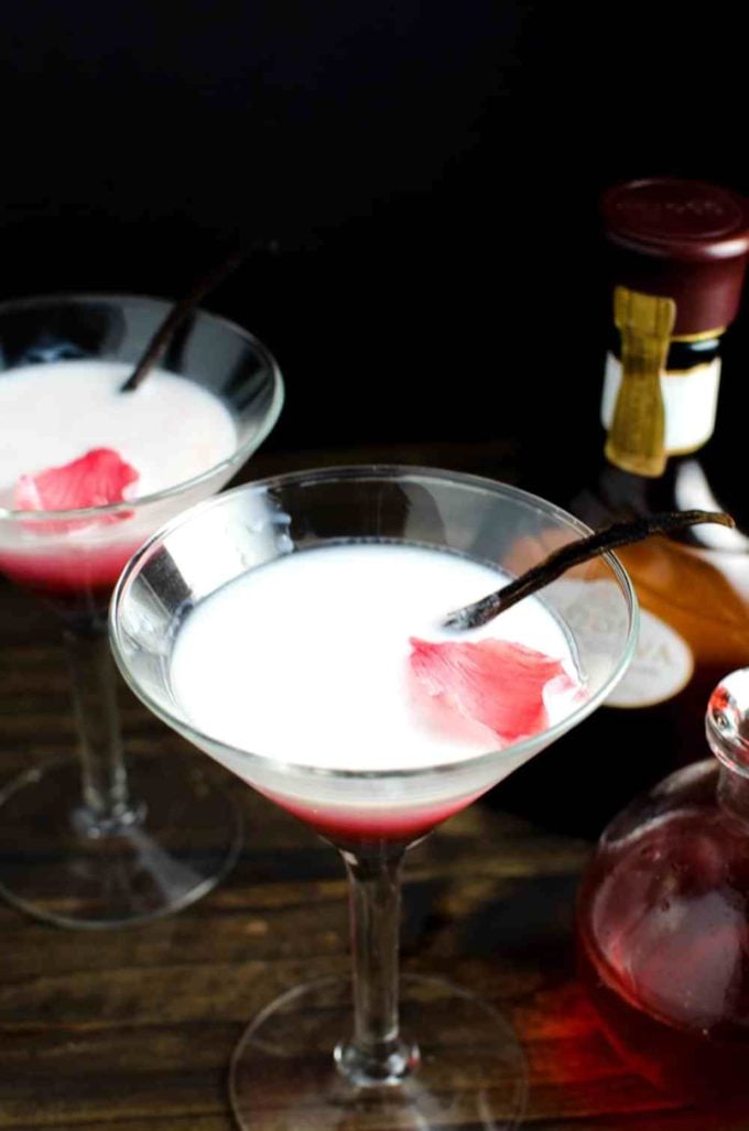 Rose and White Chocolate Cocktail in a martini glass with a rose petal and vanilla bean in each one. 