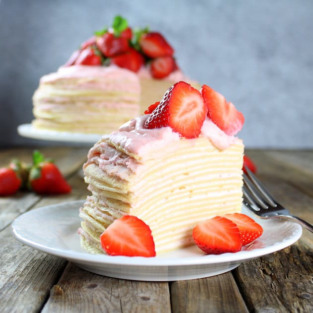 Strawberry Lemon Creme Crepe Cake with layers of crepes covered in pink icing and topped with sliced strawberries. 