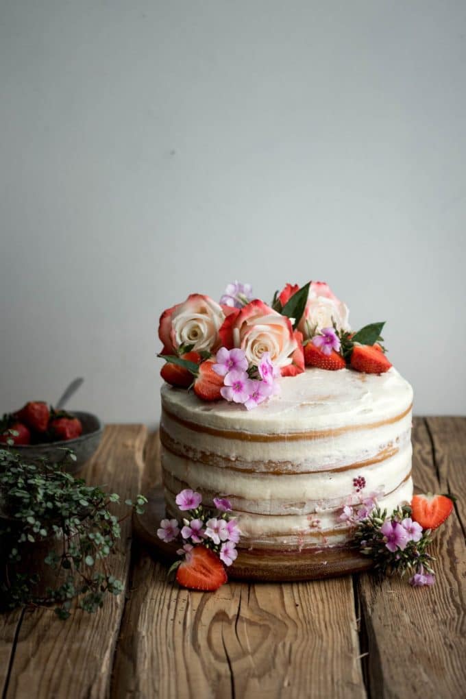 Vanilla and Berry Layer Cake topped with roses and other flowers plus sliced strawberries. 