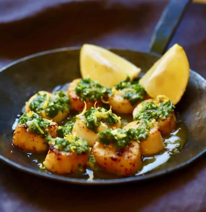 Pan Seared Sea Scallops in a cast iron pan topped with salsa verde