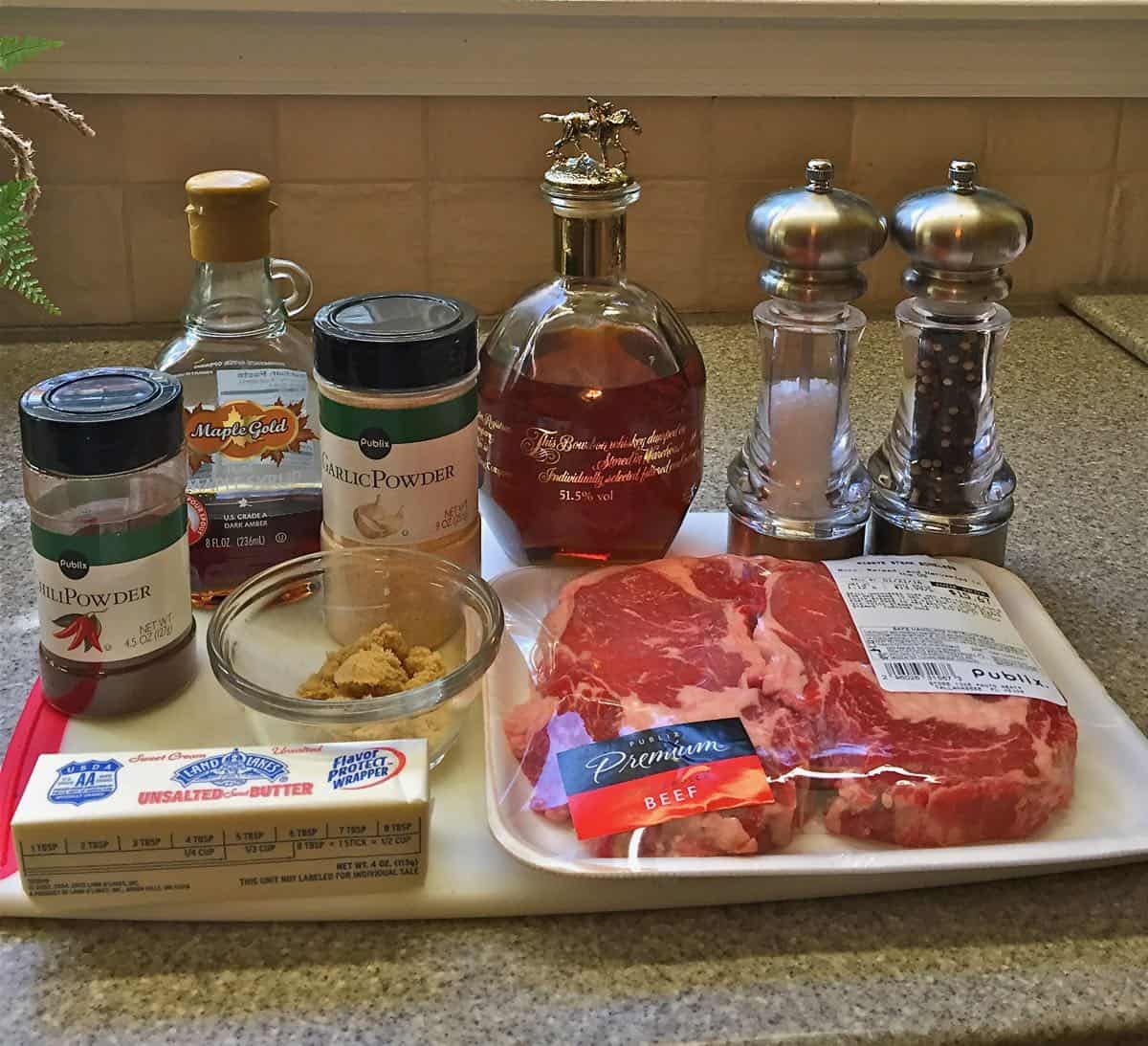 A package of ribeye steaks, butter, salt and pepper, garlic salt and chili powder on a cutting board.