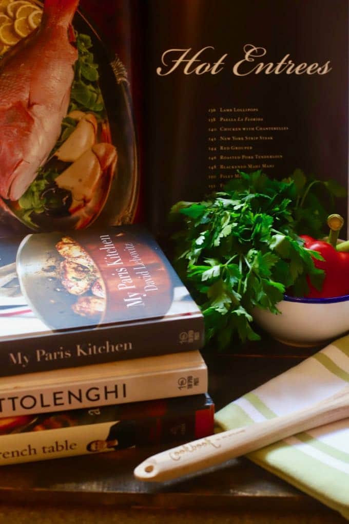 A stack of cookbooks next to a bowl of vegetables