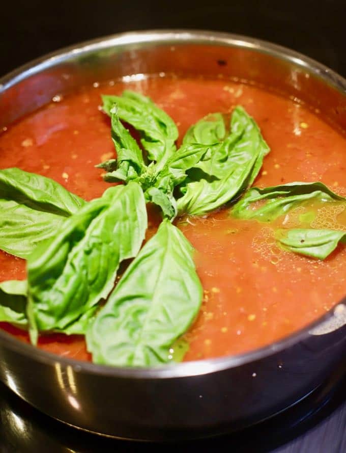 Adding a whole sprig of basil to homemade marinara sauce for Easy Stuffed Shells with Marinara Sauce