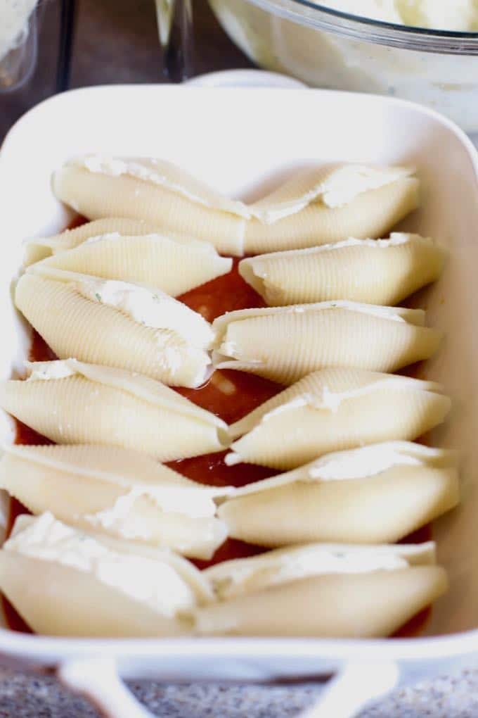 Stuffed pasta shells in a thin layer of sauce in a baking dish for Easy Stuffed Shells with Marinara Sauce