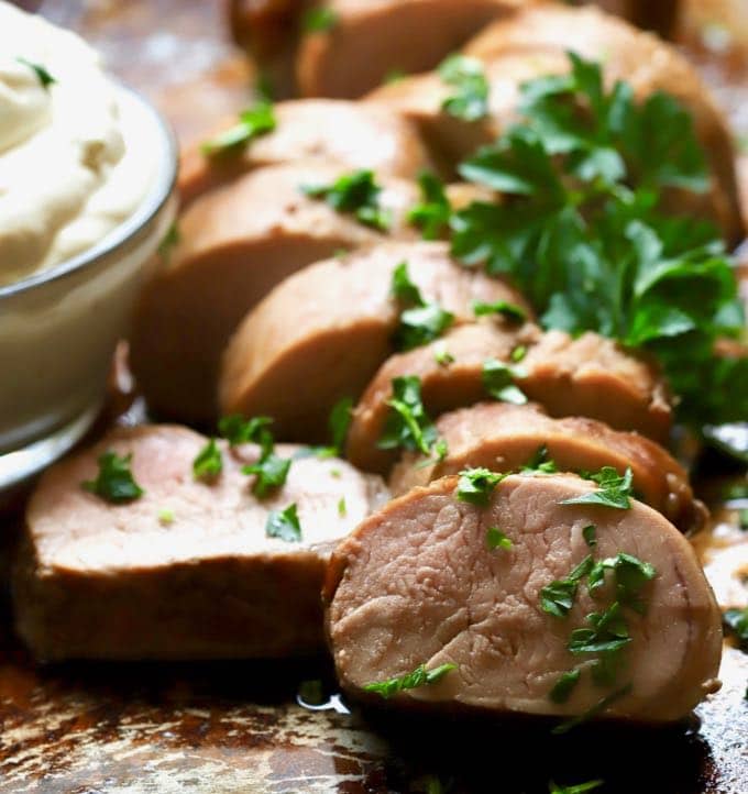 Sliced cooked pork tenderloin on a baking sheet garnished with parsley. 