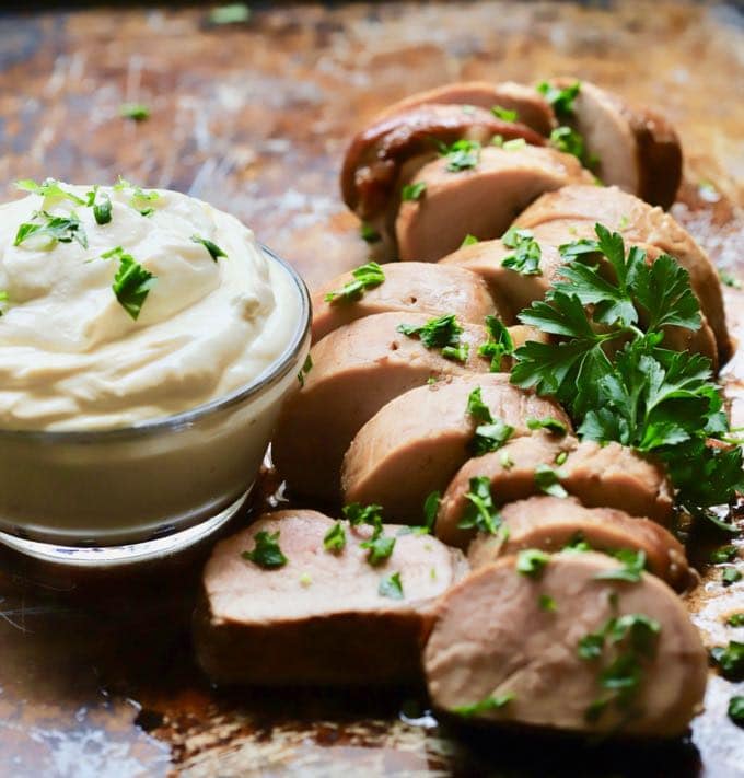 Sliced Pork Tenderloin with Mustard Sauce garnished with parsley on a baking sheet