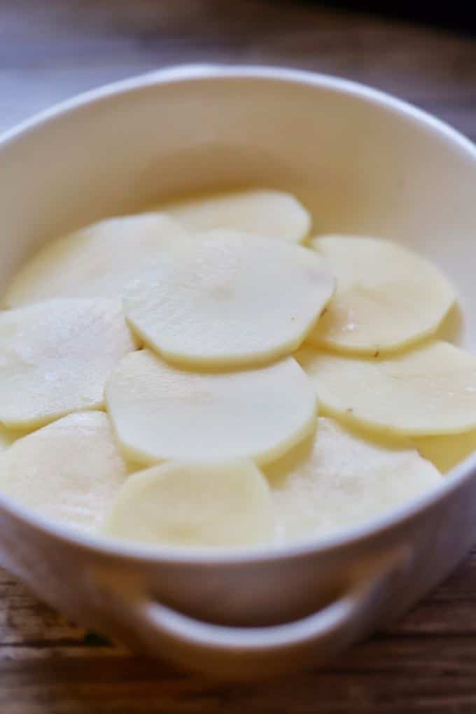 A layer of potatoes in a white baking dish for Southern Cheesy Scalloped Potatoes
