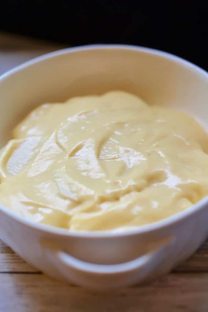 A layer of cheese sauce over a layer of potatoes in a baking dish for Southern Cheesy Scalloped Potatoes