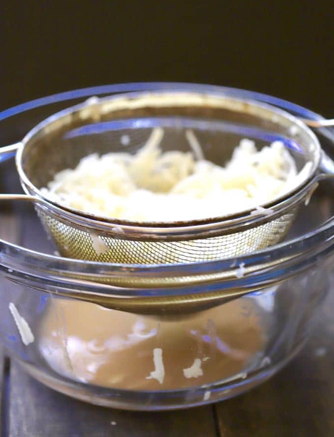 Draining grated raw potatoes in a wire strainer to remove excess liquid.