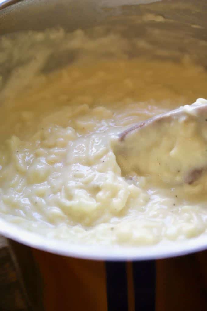 Mixing mashed potatoes, raw grated potatoes, and flour mixture together in a glass bowl.