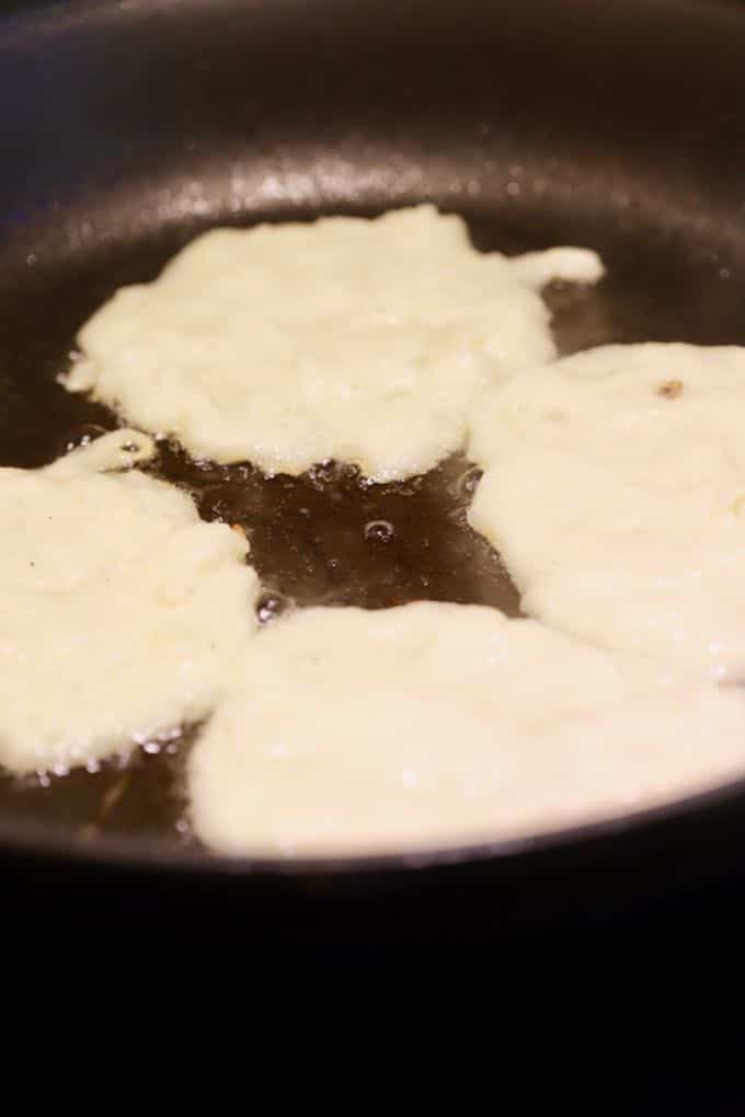 Dropping potato mixture batter into a skillet for potato pancakes.