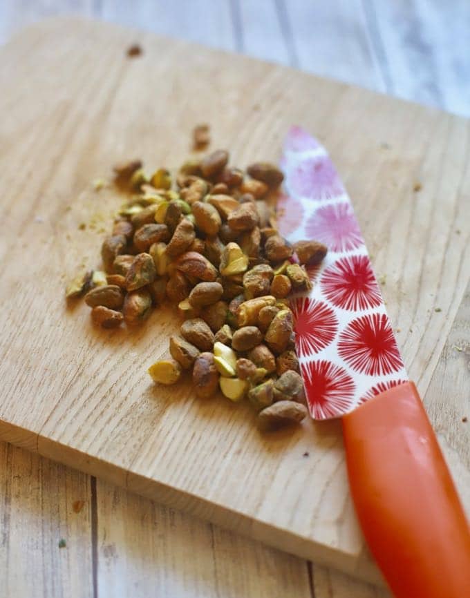 Chopped pistachios on a cutting board with a fancy knife.