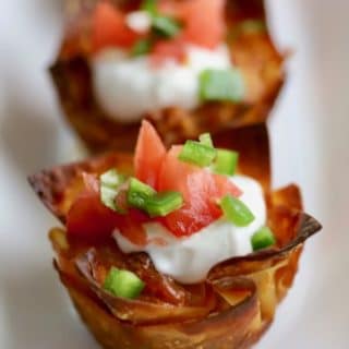 Close up of an Easy Crunchy Taco Cup on a white plate garnished with a dollop of sour cream and Pico de Gallo
