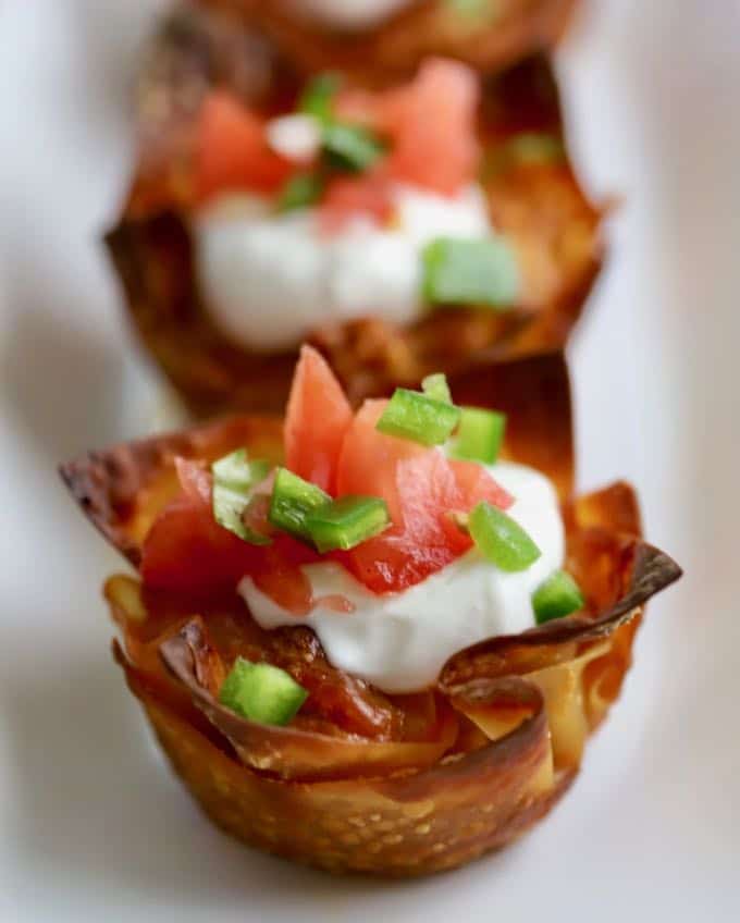 Close up of an taco cups on a white plate garnished with a dollop of sour cream and Pico de Gallo